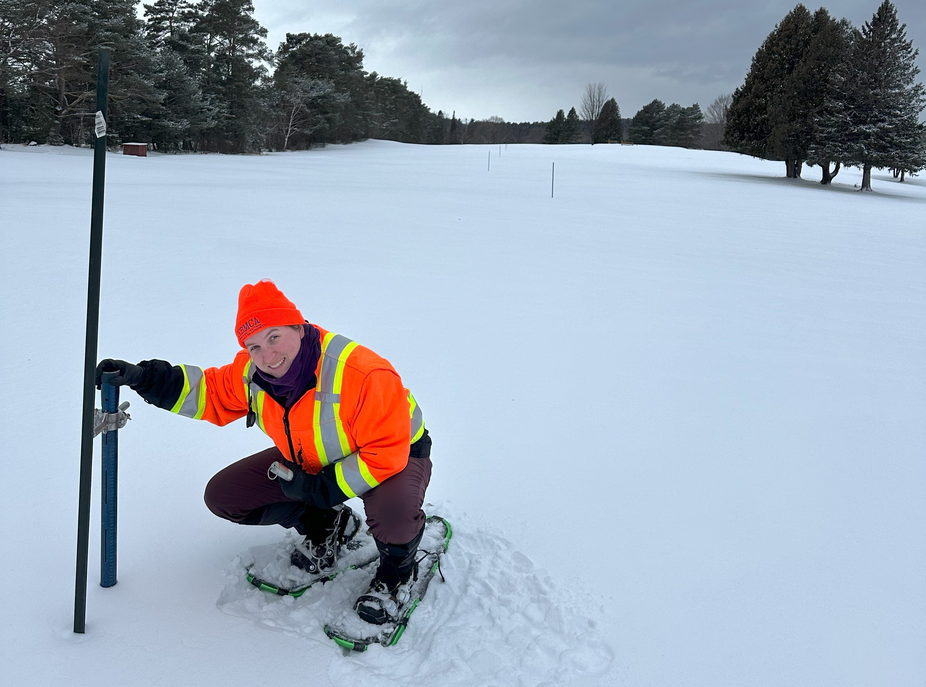 Woman in the winter on the golf course next to snow survey equipment, measuring snow depth